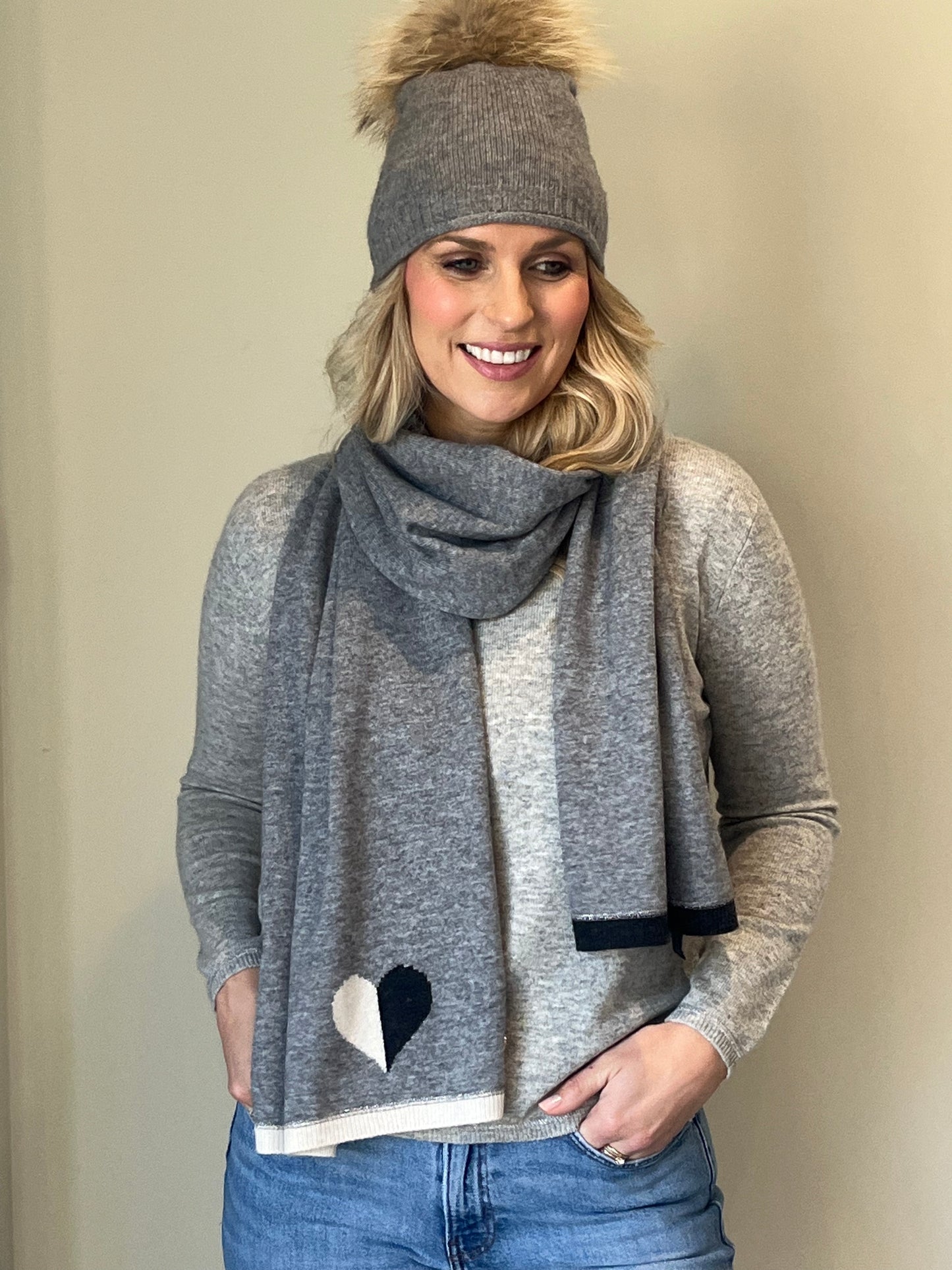 Grey cashmere plain knit beanie with faux fur pom and matching grey scarf with black & winter white intarsia heart design and end trim