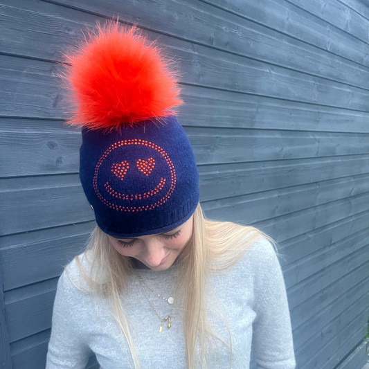 Navy cashmere plain knit beanie with an orange smiley embellishment & faux fur pom